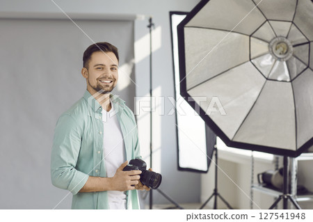 Portrait of handsome photographer posing with his camera in office Portrait of handsome photographer posing with his camera in office 127541948