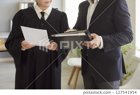 Judge woman in professional outfit standing engaged in reviewing documents in court room Judge woman in professional outfit standing engaged in reviewing documents in court room 127541954