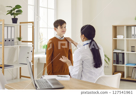 Smiling woman pediatrician examining preteen boy patient in medical office 127541961