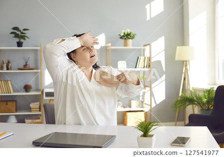Overweight woman suffering from summer heat and refreshing herself with paper fan 127541977