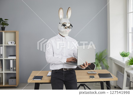 Business man in funny rabbit mask standing in office and working on laptop computer 127541998