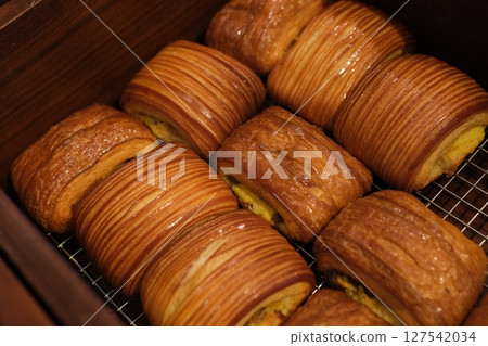 Golden layered pastry on plate in natural light With puffed edges and a delicate sugar coating, these pastries evoke a rustic charm perfect for breakfast or dessert. 127542034