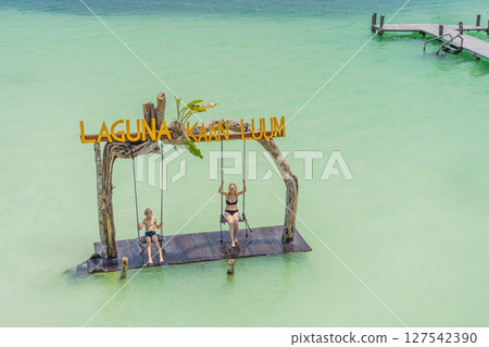 Mother and son swinging over the turquoise waters of Kaan Luum Lagoon, Quintana Roo, Mexico. Family bonding and tropical adventure concept 127542390