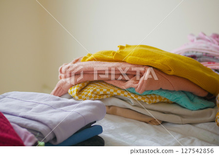 Neatly folded clothes stacked on a bed in a cozy room 127542856