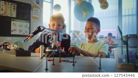 Team of Multiethnic Talented Boys Sitting at Table, Studying Robotic Arm Model Team of Multiethnic Talented Boys Sitting at Table, Studying Robotic Arm Model 127543448