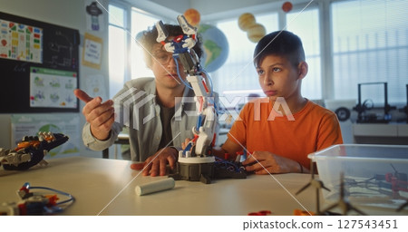 Elementary School Student Studying Model of Innovative Robotic Arm. Teacher Educating Smart Boy Elementary School Student Studying Model of Innovative Robotic Arm. Teacher Educating Smart Boy 127543451