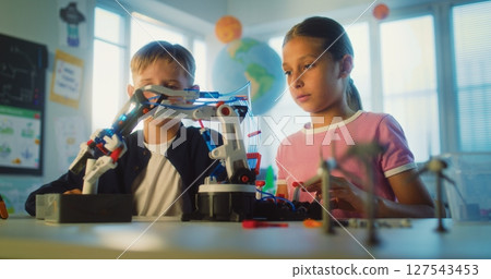 Team of Talented Boy and Girl Sitting at Table, Studying Robotic Arm Model During Science Lesson Team of Talented Boy and Girl Sitting at Table, Studying Robotic Arm Model During Science Lesson 127543453