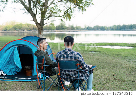 Gay LGBTQIA couple sitting on picnic chair drinking tea and coffee while camping on vacation holiday Gay LGBTQIA couple sitting on picnic chair drinking tea and coffee while camping on vacation holiday 127543515
