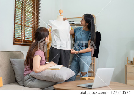 Asian woman friends couple talk to camera to sell the clothes at home. Young attractive business people female live streaming and showing clothing to customer in online 127543525