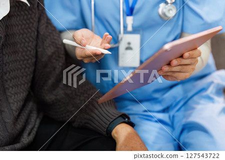 Doctor or nurse caregiver showing prescription or document and holding drug bottle to senior man at home or nursing home 127543722