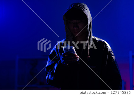 Young Man in Hoodie looking at his smart phone in Dark Tech Environment 127545885