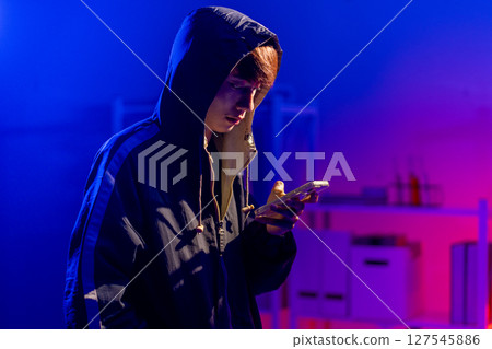 Young Man in Hoodie looking at his smart phone in Dark Tech Environment 127545886