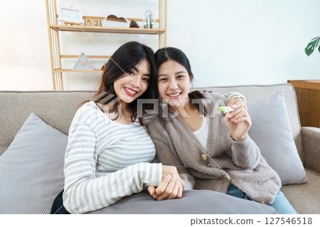 Two happy gay lesbian lgbt women couple sitting on sofa celebrating positive pregnancy test. lgbtq concept 127546518