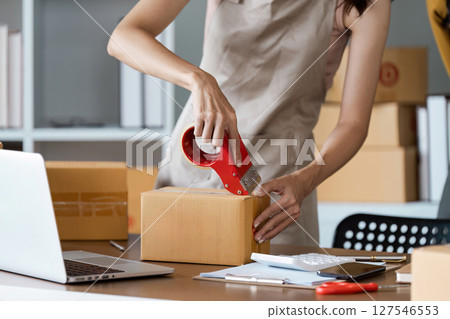 Young business entrepreneur sealing a box with tape. Preparing for shipping, Packing, online selling, e-commerce concept Young business entrepreneur sealing a box with tape. Preparing for shipping, Packing, online selling, e-commerce concept 127546553