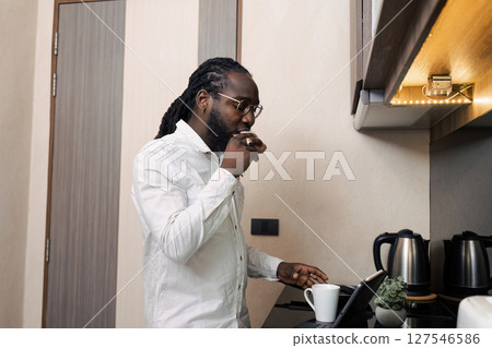 African businessman eat sandwich in the morning and use a tablet to work on company documents. While working online from home 127546586