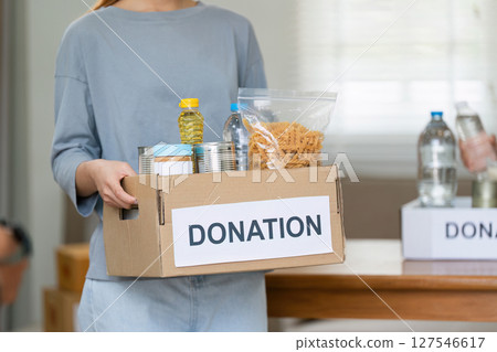 charity, donation and volunteering concept. Volunteer prepare foodstuff box containing food to donate to people poor, disaster victim at home charity, donation and volunteering concept. Volunteer prepare foodstuff box containing food to donate to people poor, disaster victim at home 127546617