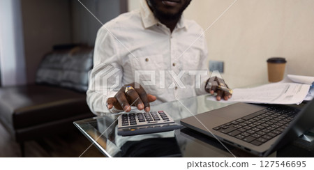 Business African man using a calculator to calculate numbers on a company's financial documents at home. work from home concept 127546695
