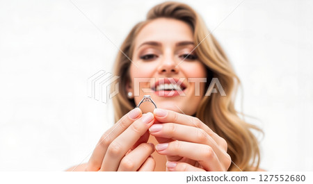 Woman smiling while holding engagement ring against white background 127552680