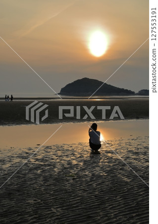 A woman looks at the tide pools at Chichibugahama Beach in Mitoyo, where the setting sun is reflected 127553191