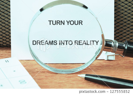 TURN YOUR DREAMS INTO REALITY words focused on the notebook through a magnifying glass TURN YOUR DREAMS INTO REALITY words focused on the notebook through a magnifying glass 127555852