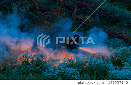 The fireman is able to put out a forest fire that has lots of smoke and fire 127557140