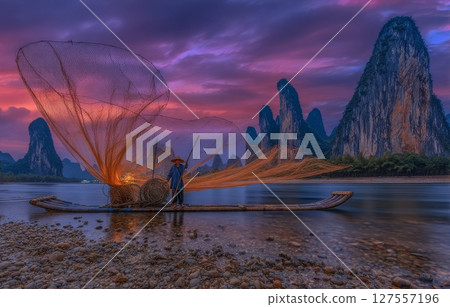 Xingping, China, is where a cormorant fisherman can be seen throwing a net from a traditional Chinese bamboo boat at the break of day 127557196
