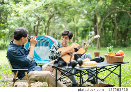 Family bonding during camping. Father and son enjoying music together outdoors. Family bonding during camping. Father and son enjoying music together outdoors. 127563716