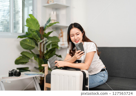 Travel planning. Young woman checking details on smartphone while preparing for a trip. 127563724
