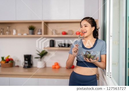 ESG and Healthy Choices. Smiling woman with a salad by the window in a bright kitchen. 127563727