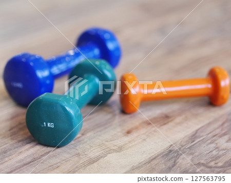 Three dumbbells of different colors and weights are on a wooden floor 127563795