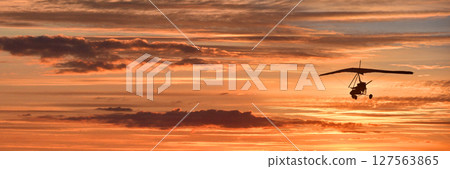 Hang glider on a motor on a summer evening against the backdrop of a sunset sky. Extreme sport. Banner, blank for an advertising layout with a place for writing Hang glider on a motor on a summer evening against the backdrop of a sunset sky. Extreme sport. Banner, blank for an advertising layout with a place for writing 127563865