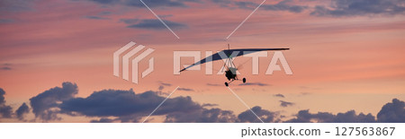 Hang glider on a motor on a summer evening against the backdrop of a sunset sky. Extreme sport. Banner, blank for an advertising layout with a place for writing 127563867