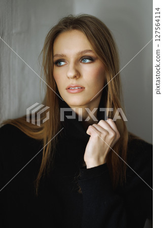 Stunning woman in black sweater, exuding quiet power and grace, her delicate hand gesture and captivating gaze creating cinematic aura, highlighted by soft light that accentuates her timeless beauty 127564114