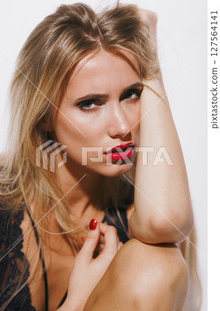 emotions and feelings concept - sensual blonde woman in lingerie, experiencing pure pleasure, body arching, mouth open in ecstasy, her glowing skin bathed in bright light against a white backdrop 127564141