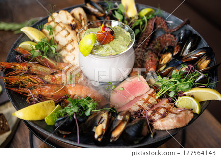 Grilled seafood platter with mussels, shrimp, octopus, and seared tuna. Served with fresh herbs, lemon wedges, and creamy avocado sauce with caviar. Exquisite gourmet dish in a fine dining restaurant 127564143