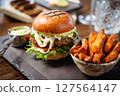 Gourmet veggie burger with lettuce, tomato, cheese, and sauce on a brioche bun. Served with a side of crispy sweet potato fries and a small cup of sauce. Vegetarian meal served in modern restaurant 127564147