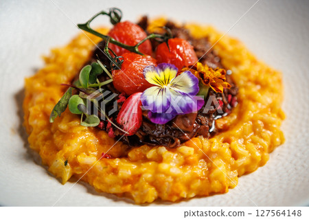 Creamy saffron risotto topped with braised beef, roasted cherry tomatoes, and edible flowers. Delicious gourmet Italian cuisine served in a modern restaurant setting 127564148