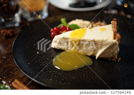Rich cheesecake slice with a buttery crust, highlighted by a lemon sauce drizzle. Garnished with mint, red currants, and crumble. Gourmet dessert closeup in an upscale restaurant 127564149