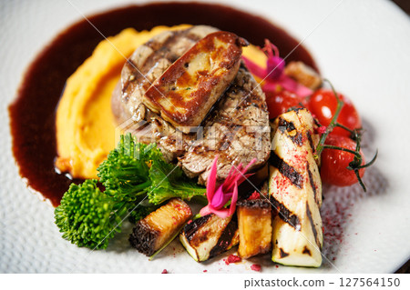 Succulent beef filet with foie gras, served with velvety mashed sweet potatoes, grilled zucchini, and cherry tomatoes. A gourmet meal in a sophisticated dining setting 127564150