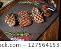 Juicy grilled steaks with Brazilian, Uruguayan, and Estonian flags. Served with fresh herbs and microgreens on a slate plate, showcasing international gourmet cuisine in a fine dining setting 127564153