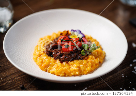 Rich saffron risotto with tender braised beef, roasted cherry tomatoes, and vibrant edible flowers. Exquisite Italian dish presented beautifully for a fine dining experience 127564154