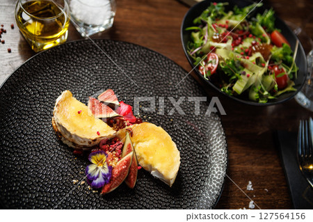 Cheese plate with figs and edible flowers. Fresh salad with tomatoes and greens. Fine dining presentation in a modern restaurant. Healthy and delicious gourmet meal closeup 127564156