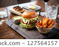 Vegetarian burger with fresh greens, tomato, cheese, and creamy sauce on a brioche bun. Accompanied by a bowl of sweet potato fries and a metal cup of dip. Healthy and tasty dining option 127564157