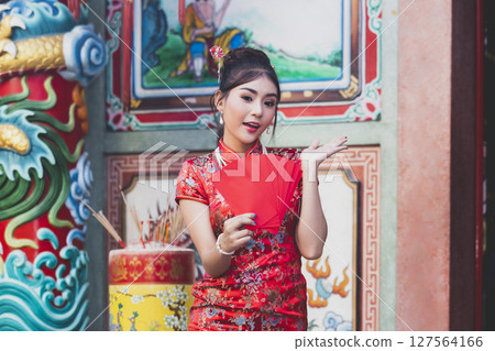 Chinese woman in a red cheongsam (qipao) dress holding red envelopes (hong bao) at shrine. Concept to celebrate Chinese New Year. 127564166
