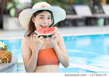 Very Beautiful woman relaxing in swimming pool and eating watermelon. Sexy young asian woman in swimsuits in summer. 127564170