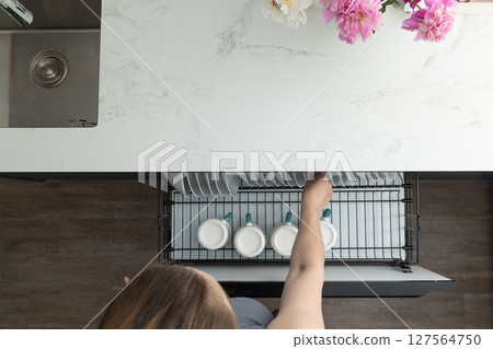 Organizing Clean Dishes in a Modern Kitchen With Floral Decoration on the Counter Organizing Clean Dishes in a Modern Kitchen With Floral Decoration on the Counter 127564750