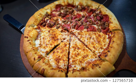 Delicious pizza featuring a combination of cheese and meat lovers toppings, served on a wooden board. The golden cheese stuffed crust 127565710