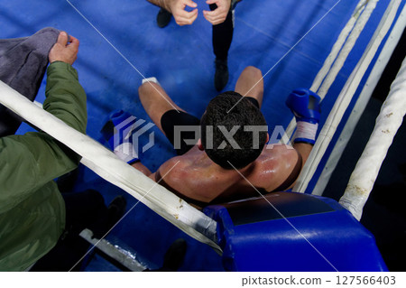 Top view of cornered boxer receives strategic advice from trainer during intense bout. 127566403