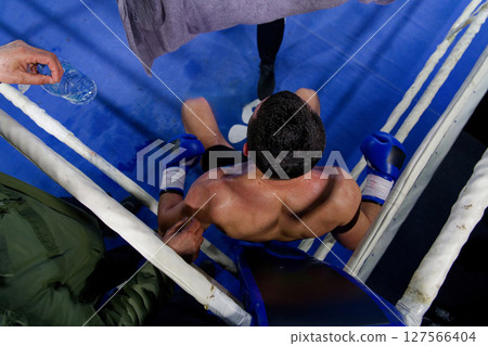 Top view of cornered boxer receives strategic advice from trainer during intense bout. 127566404