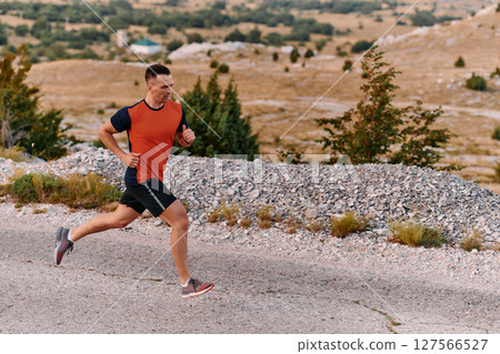 Determined Athlete Running Through Rugged Mountain Terrain at Sunrise. 127566527